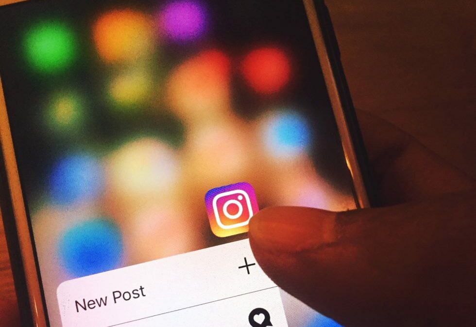 Closeup of a cellphone and someone's thumb tapping on the Instagram logo